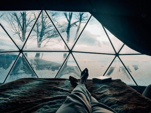 a person laying on a bed in front of a glass window at Dômes Charlevoix in Petite-Rivière-Saint-François