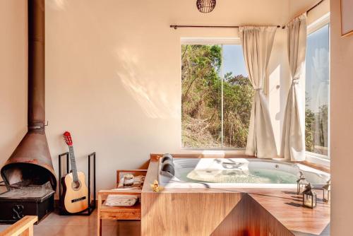 a bath tub in a room with a window and a guitar at Vivenda Apua Chalés in Piracaia