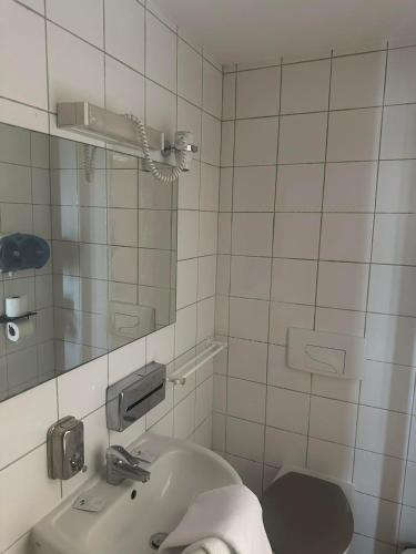 a white tiled bathroom with a sink and a mirror at Hôtel Victoria in Reims