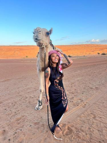 a woman standing next to a camel in the desert at R61 Sunset Chalet in Muntarib