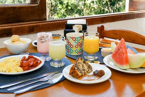 a table with plates of food and glasses of juice at VELINN Pousada Torre Branca in Monte Verde