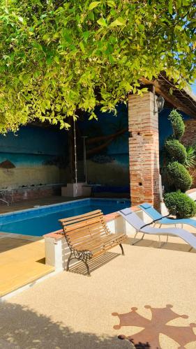 un banc assis sous un arbre à côté d'une piscine dans l'établissement Studio Au Clos Saint Georges , piscine et Spa, à Saint-Jory