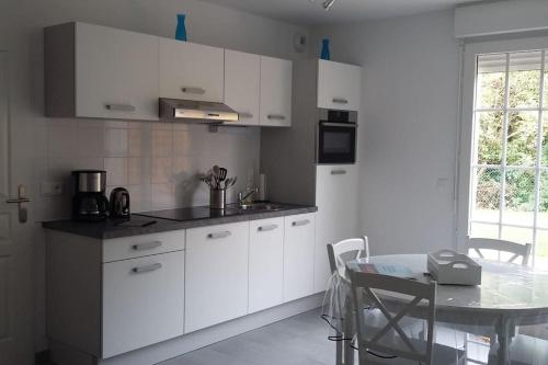 une cuisine avec des armoires blanches, une table et une fenêtre dans l'établissement Maison, gîte en Baie de Somme à Saint-Valery-sur-Somme, à Saint-Valery-sur-Somme
