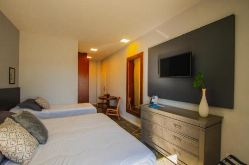 a bedroom with two beds and a tv on the wall at Hotel Villareal São Francisco do Sul in São Francisco do Sul