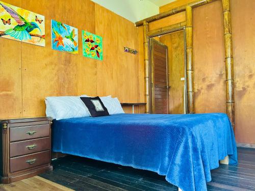 1 dormitorio con cama azul y pared de madera en Cabañas Los Gulungos Lodge, en Jardín
