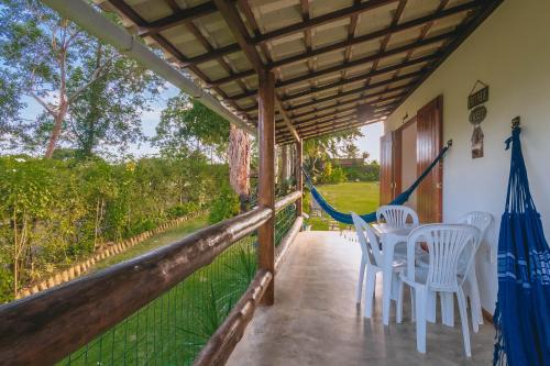 a porch of a house with white chairs and trees at Casa paradise perto da praia Guarajuba - BA in Camacari
