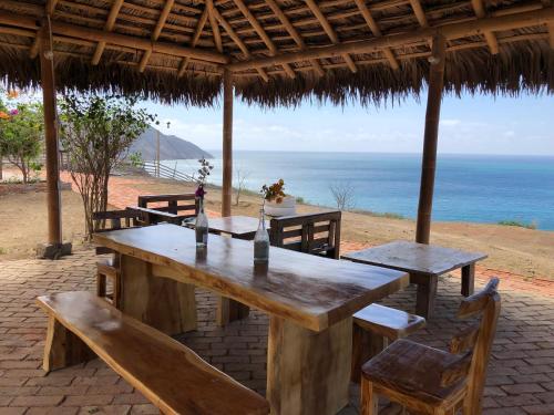 a wooden table and chairs under a hut with the ocean at Encantadora y Tranquila Casa de Playa Vista al Mar in Aromo