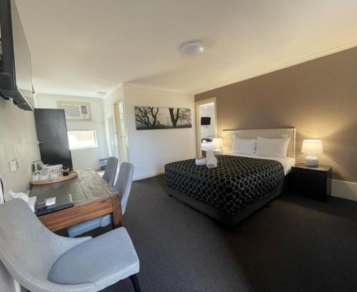 a hotel room with a bed and a desk and chairs at Fig Tree Motel in Narrandera