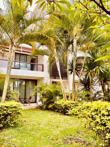 a building with palm trees in front of a yard at Belle Haven GF 1bedroom flat in Mont Choisy