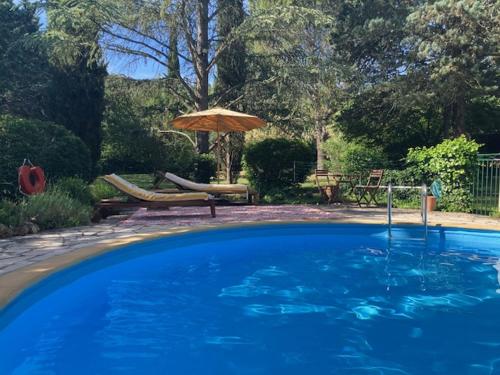 a large blue swimming pool with an umbrella and chairs at Bastide en Provence in Auriol