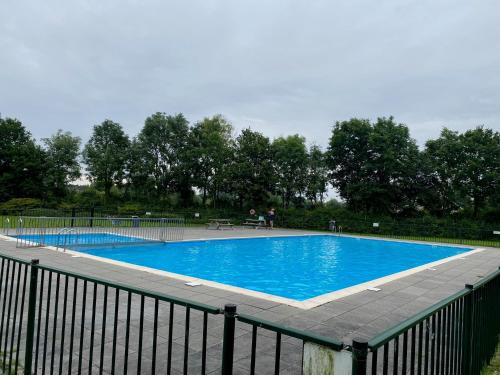 a large blue swimming pool with a black fence at Villa Riverside met hottub, eigen aanlegsteiger, zwemtrap, trampoline en kano's in Zeewolde