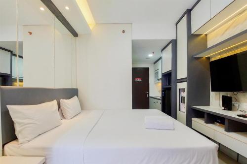 a bedroom with a large white bed and a television at Homey and Nice Studio at Transpark Bintaro Apartment By Travelio in Tangerang
