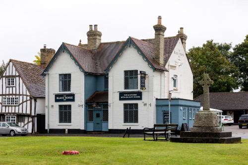 a white and blue building with a bench in the grass at The Black Horse in Swaffham Bulbeck