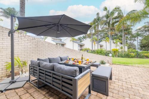 a patio with a couch and an umbrella at The Moorings 23 4 Cromarty Rd air con pool and waterfront in Soldiers Point