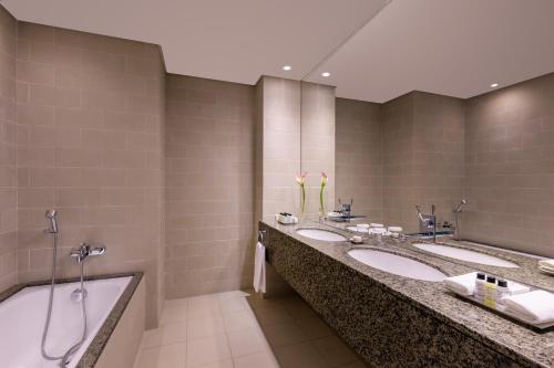 a bathroom with three sinks and a bath tub at Grand Millennium Al Wahda Hotel and Executive Apartments Abu Dhabi in Abu Dhabi