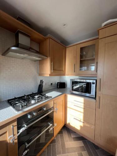 a kitchen with wooden cabinets and a stove top oven at Cosy 2 Bed Service Apartment Netflix Hideaway Family Couples Staycation Tredegar Park Celtic Manor ICC Wales in Lower Clapton