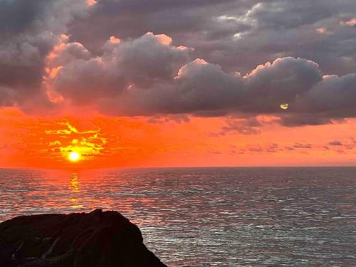 a sunset over the ocean with a rock in the foreground at Casual comfort in Byron Shire in Mullumbimby