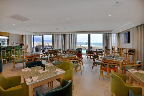 a restaurant with tables and chairs and windows at Lagoon Beach Hotel & Spa in Cape Town
