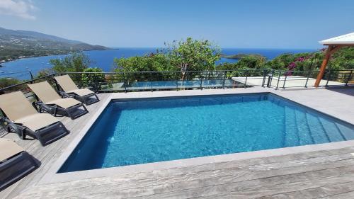 een zwembad met stoelen en uitzicht op het water bij Villa 4 étoiles Le Roc de Malendure in Bouillante