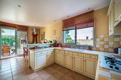 une grande cuisine avec des placards jaunes et une grande fenêtre dans l'établissement La Villa Noémie - À 10mn de Perpignan, à Saleilles