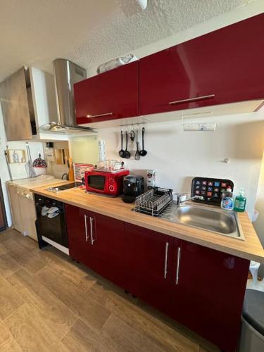 La cuisine est équipée de placards rouges et d'un plan de travail avec évier. dans l'établissement Appartement Cap d'Agde accès direct à la plage, au Cap d'Agde