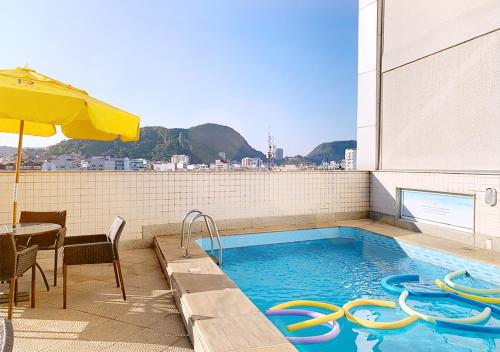 a swimming pool with a table and an umbrella at Riale Vilamar Copacabana in Rio de Janeiro