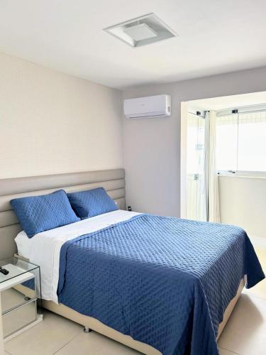 a bedroom with a bed with blue sheets and a window at Apartamento de Luxo em Guarapari in Guarapari