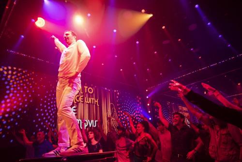 a man standing on a stage in front of a crowd at The LINQ Hotel & Casino, A Caesars Destination in Las Vegas
