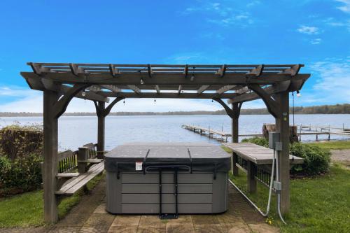 a picnic table under a pergola next to the water at 3BR Fife Lake Getaway with Fire Pit & Hot Tub in Fife Lake