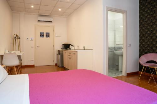 a bedroom with a pink bed and a kitchen at LHE Les Trois Merveilles in Cesena
