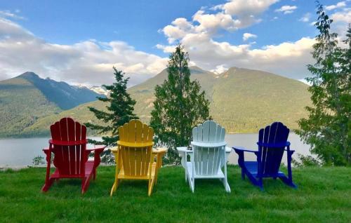 four colorful chairs sitting in the grass near a lake at The Sentinel in Kaslo