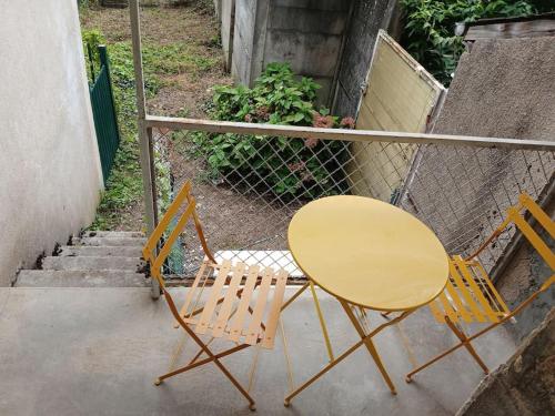 two chairs and a yellow table next to a fence at Petite maison studio cosy avec jardin in Saint-Honoré-les-Bains