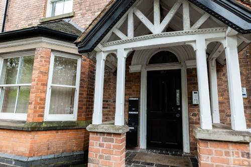 a brick house with a black door with white columns at Luxury Modern Flat In Wolverhampton- Garden Views in Wolverhampton