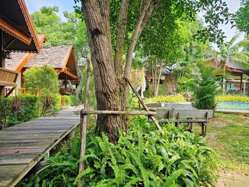 a wooden walkway next to a tree with a bench at Siri Lagoona Resort in Nong Prue