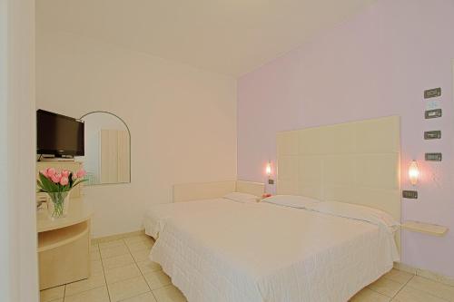 a white bedroom with a bed and a tv at Hotel Flora in Milano Marittima