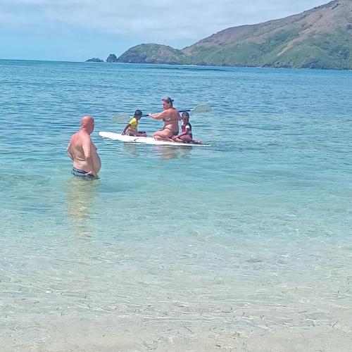 a group of people sitting on a surfboard in the water at Max's Beachside homestay room 2 in Nalauwaki