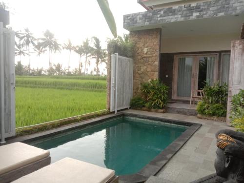 a swimming pool in front of a house with a rice field at Sujiwa Ubud Hotel & Villa in Ubud