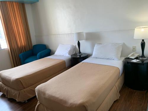 a hotel room with two beds and a blue chair at Pearl Manila Hotel in Manila