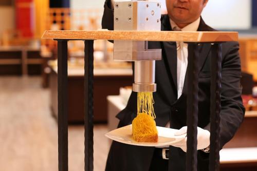 a man in a suit is producing food on a machine at Hotel Sakurai in Kusatsu