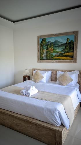 a large bed with white sheets and a painting on the wall at Sujiwa Ubud Hotel & Villa in Ubud