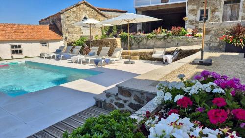 a swimming pool with chairs and umbrellas and flowers at Casas São Tiago - Arouca, conforto e natureza in Arouca