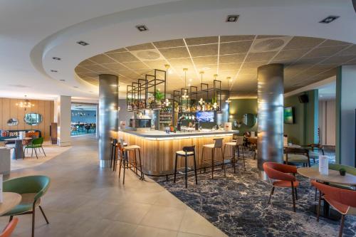 a restaurant with a bar with chairs and tables at Novotel Bourges in Bourges