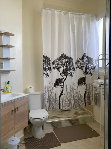 a bathroom with a toilet and a shower curtain with trees at Appartement cosy à 5 min de la plage Sidi Kacem in Hajreien