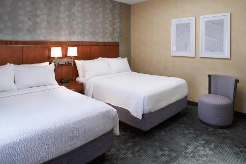 a hotel room with two beds and a chair at Courtyard Detroit Dearborn in Dearborn