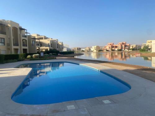 a large blue swimming pool next to a body of water at Sunset Haven in Tawila TownHouse in Hurghada
