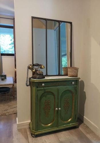 un meuble vert avec un miroir et un téléphone dans l'établissement Mon Studio en bordure de forêt, Golf St-Germain, à Poissy