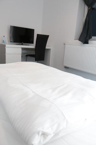 a white bed with a desk and a television at Holsteiner Hof in Heist