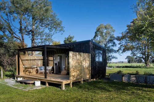 a black tiny house with a porch in a field at One77 Rural Retreat in Matarawa