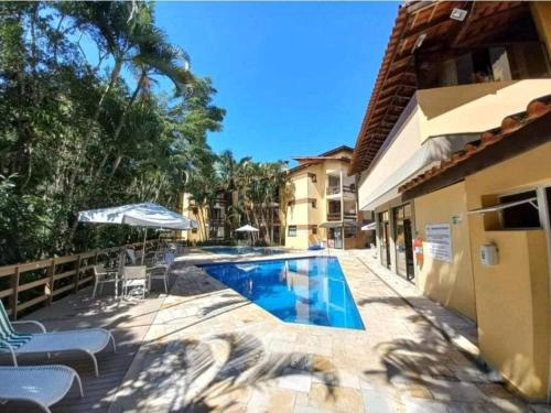 a swimming pool with chairs and an umbrella next to a building at Riviera de São Lourenço Apto Completo com Churrasqueira Serviço de Praia Piscina aquecida Sauna salão de jogos e quadra in Riviera de São Lourenço