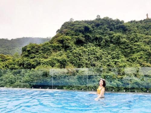 a woman in a swimming pool with a hill in the background at Sand Hotel in Cat Ba